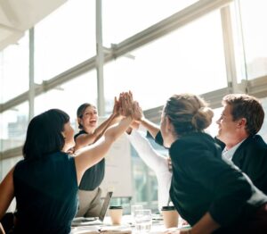 A group of people in a business meeting, celebrating with a group high-five.