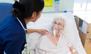 A Filipino nurse attending to an elderly patient in a hospital bed.