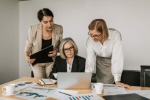 Three professional women in a discussion, looking at a laptop.