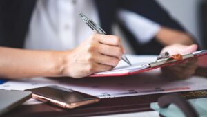 A person writing on a clipboard with a pen. 