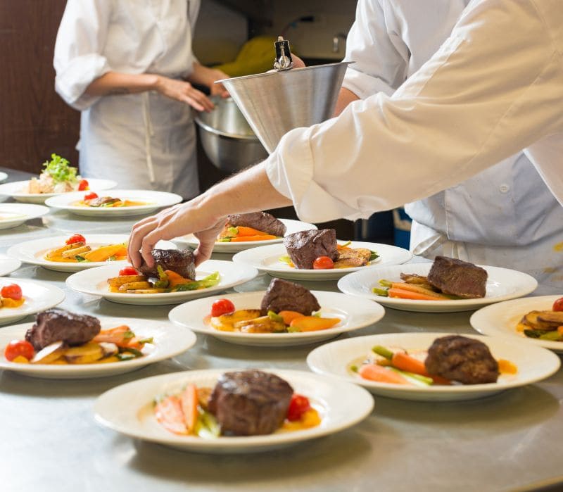 Chef plating multiple steak dishes in a professional kitchen