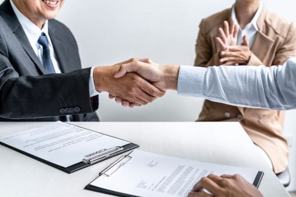 Two professionals shaking hands over a signed contract.