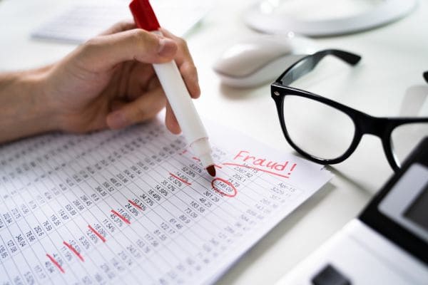 Hand marking a financial statement as fraudulent with a red pen.