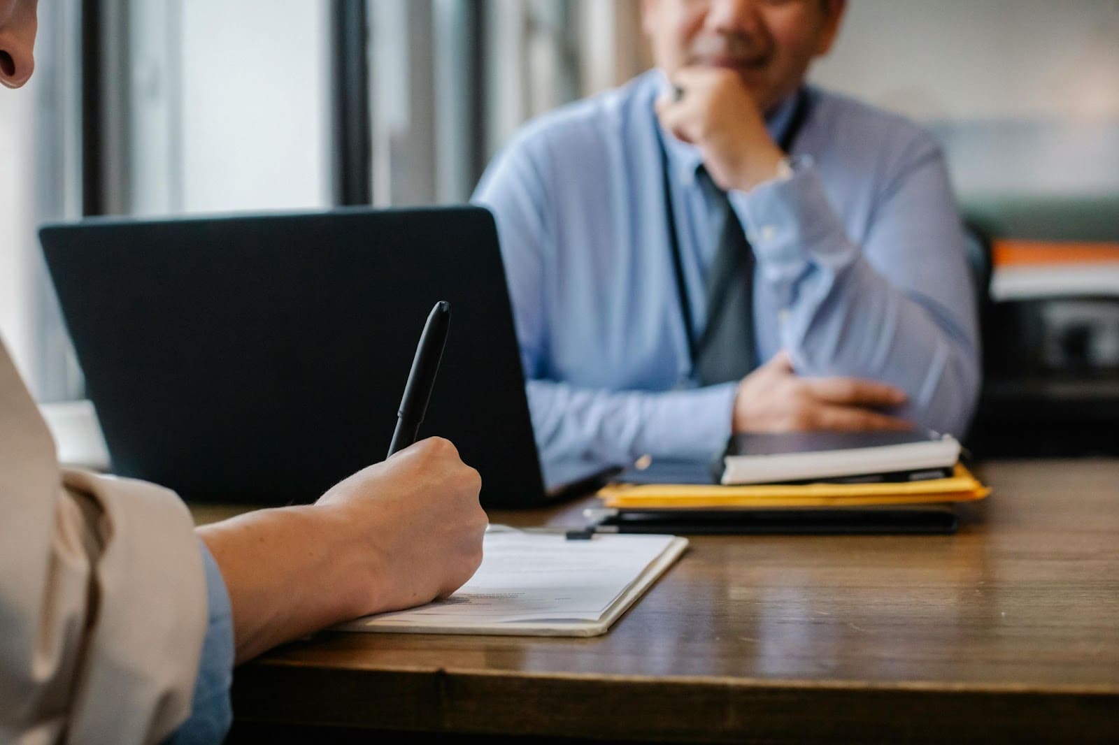 Close-up of a job interview, with one person taking notes while the other is seated in front of a laptop.