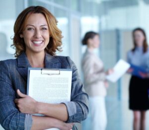 Smiling woman holding a clipboard in a professional setting.