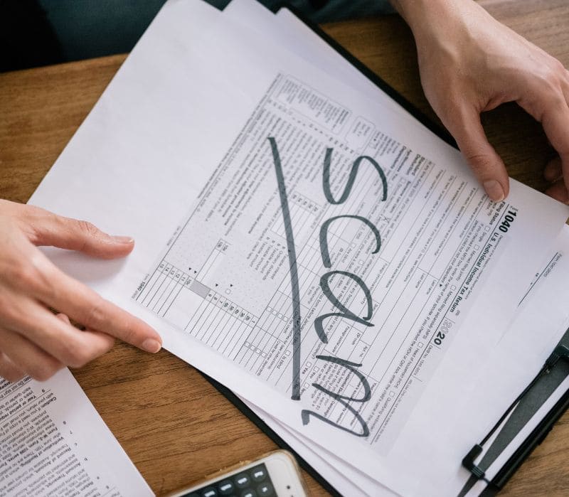 Person holding tax documents with the word 'Scam' written on top.