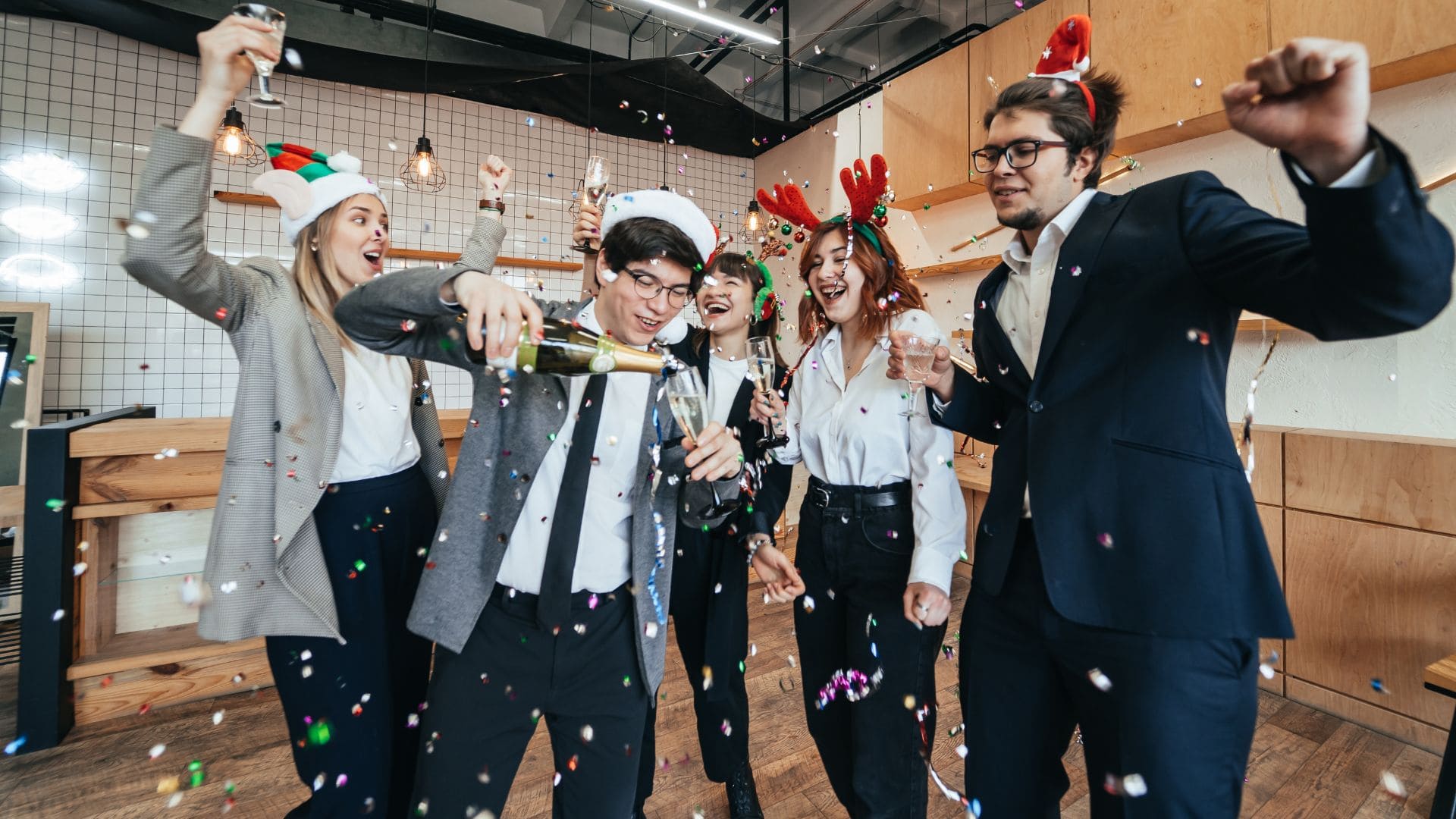 Group of people celebrating in office with Santa hats and confetti