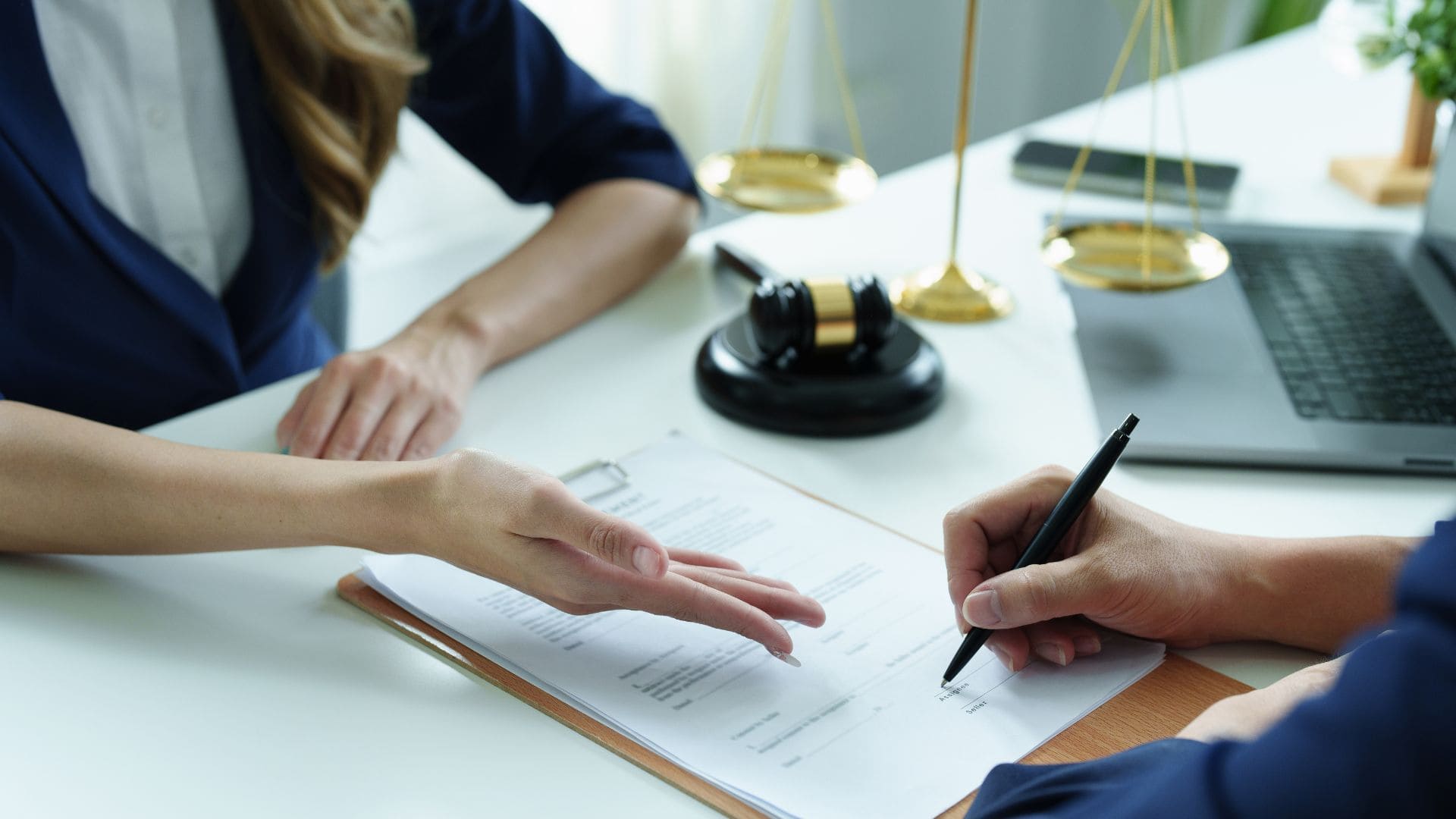 Hands signing a document with legal scales and gavel in the background