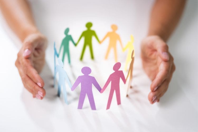 Hands surrounding paper cut-out figures of people in different colors.