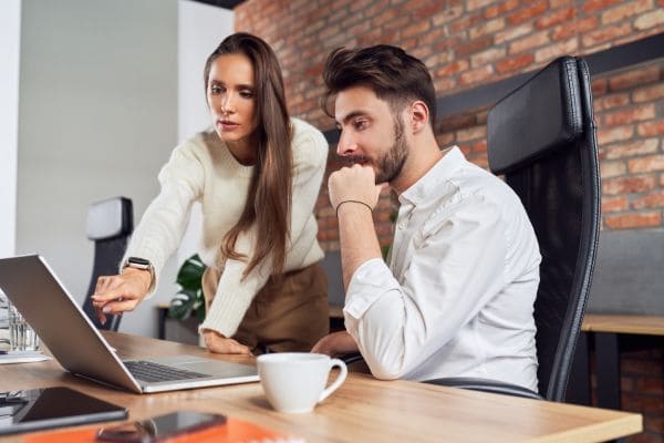 A woman explaining work on a laptop to a colleague in an office.