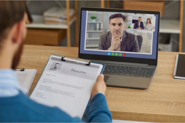 A recruiter holding a resume while conducting an online interview with a male candidate.